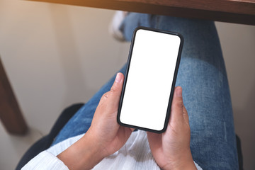 Top view mockup image of hands holding black mobile phone with blank white screen while sitting