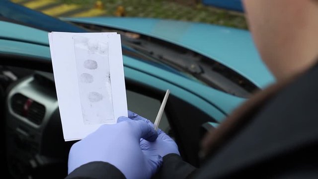 Crime Scene Unit officer collecting fingerprints and evidence on a vehicle which was damaged by criminals.