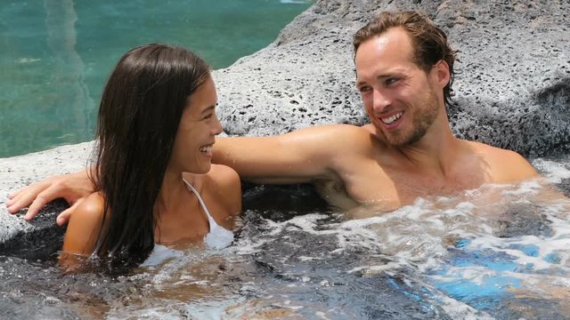 Romantic couple relaxing together in hot tub whirlpool jacuzzi luxury resort spa retreat Luxurious hotel travel vacation. People laughing talking having fun relaxed enjoying summer holidays.
