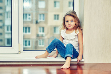 Portrait of a little girl sitting on a windowsill in the house