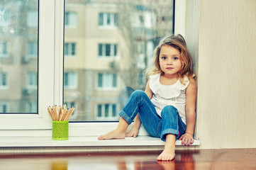 Portrait of a little girl sitting on a windowsill in the house