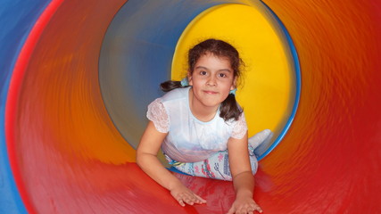 Little girl in a colored spiral tube on a playground for children, photo of a plastic pipe with curves, view from the inside