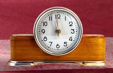 Vintage clock. Clock alarm clock with a white dial on a wooden base. Against the background of dark red cloth plaid. The clock hands are approaching midnight.