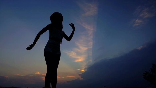 Silhouette of young attractive Latin American woman wearing hat enjoying sunset dancing on the beach