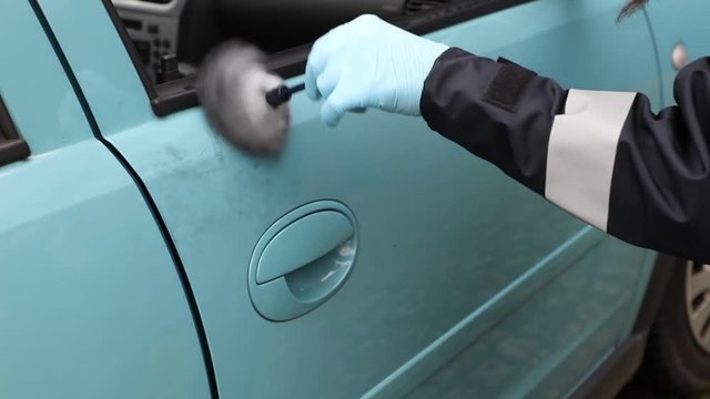 Crime Scene Unit officer collecting fingerprints and evidence on a vehicle which was damaged by criminals.