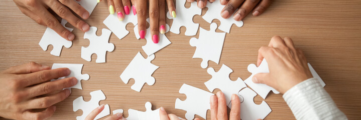 Top above close up hands diverse team assembling jigsaw puzzle joining pieces at desk search right...