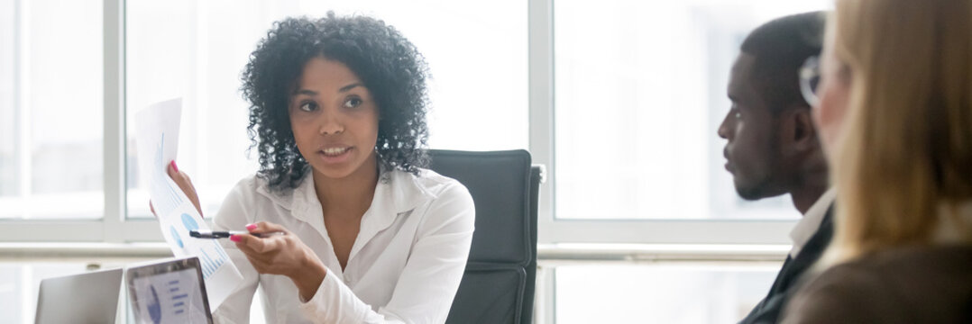 Horizontal photo multiracial people led by african businesswoman, leader showing paper financial report to clients partners negotiating at meeting sitting a boardroom, banner for website header design