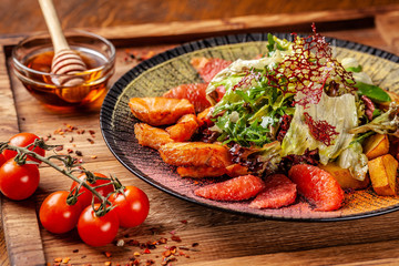 Modern Arabic cuisine in 2019. Asian salad of fried salmon, avacado, grapefruit and salad mix, with honey sauce. Serving dishes in a restaurant in a black plate with oriental spices.