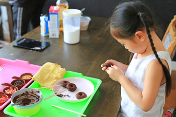 Close up little Asian kid girl in process class of homemade chocolate donuts.
