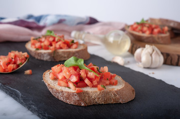 Bruschetta sandwiches with tomato, basil leaf and garlic on gray board as background