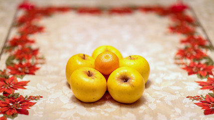 Composition of 5 apples and a mandarin forming a pyramid on the table with a flower ornament around
