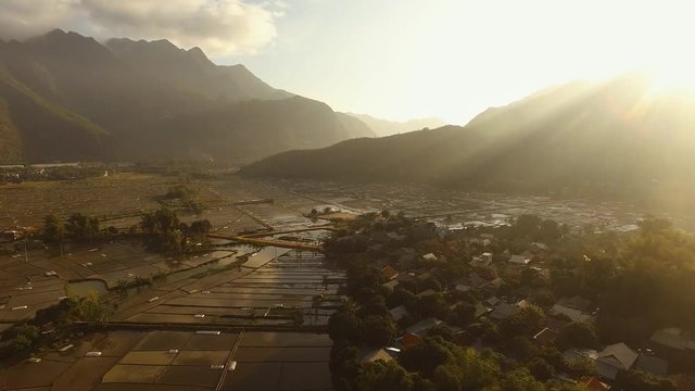 Aerial over stunning Mai Chau landscape patchwork rice paddy fields with sun breaking over mountain range.