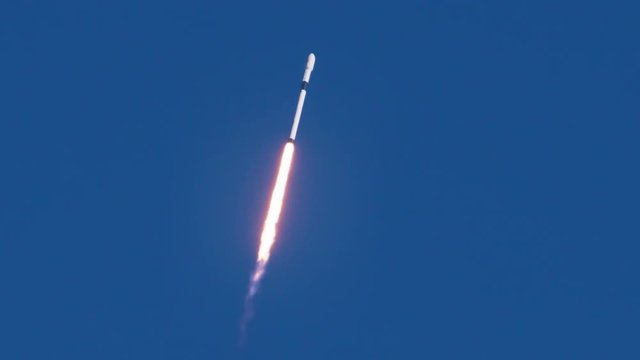 Rocket flies through clear blue sky on its way to deliver a satellite to orbit in space.  Slow motion with audio.