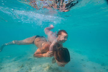 Happy mother playing with infant boy in beautiful tropical sea water with white sand, activity in vacation, underwater shot at Maldives, baby diving underwater