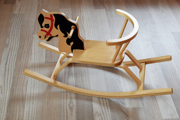 Cute wooden plywood rocking horse on brown wood texture laminate floor indoors. Children retro toy.