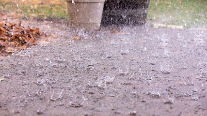 Closeup up view of a rain drops falling on a concrete patio on a background of a house. Large drops create multiple splashes.