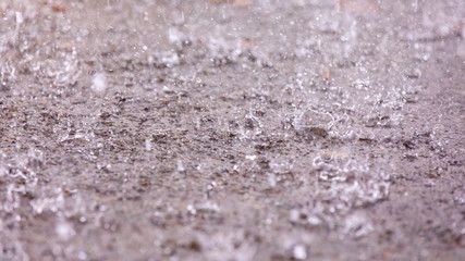 Closeup up view of a rain drops falling on a concrete patio on a background of a house. Large drops create multiple splashes.