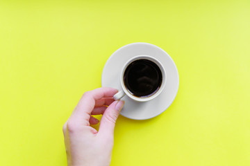 wooman's hand holding cup of coffee- top view of minimal flat lay on yellow background.