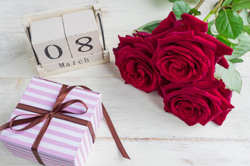 A festive gift, a wooden calendar, bouquet of red roses and a gift box on a wooden background. The concept of congratulations on March 8 or wooman's day.