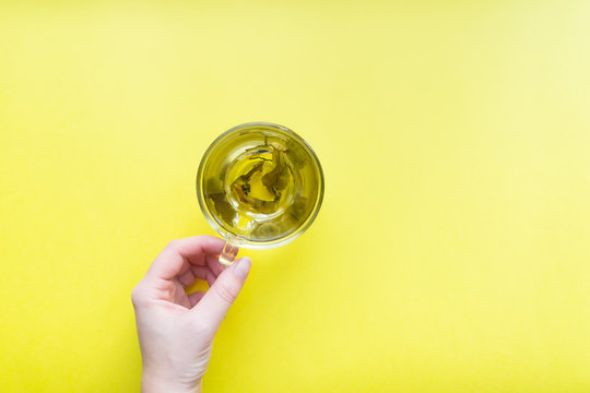 Woman's Hand Holding Cup Of Green Tea - Top View Of Minimal Flat Lay On Yellow Background.