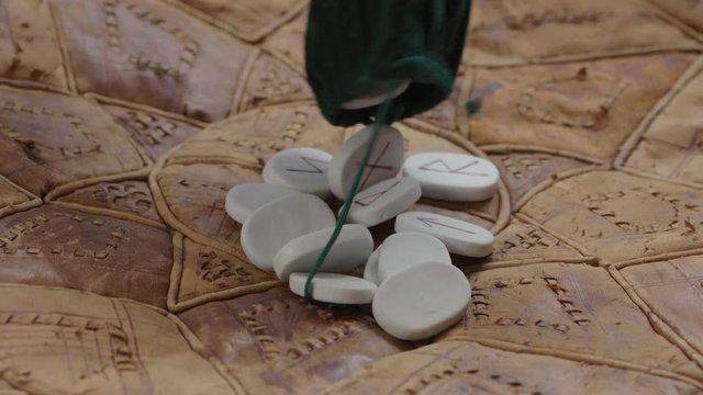 A set of smooth white rune stones drop out of a pouch onto a rustic surface