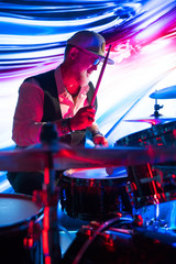 Cheerful drummer playing on drum set on stage in the color light