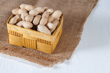 Peanuts in a wicker basket on sackcloth. White wooden background. Healthy food and health care.