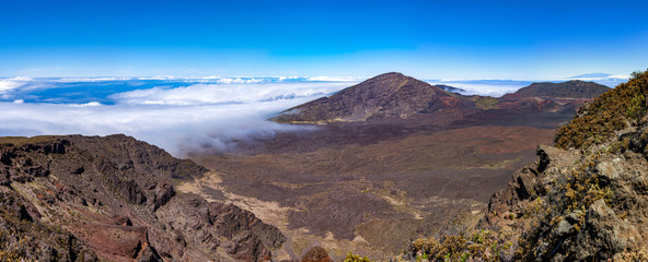 Scenic panorama of a Haleakala volcano. White clouds enters into the caldera contrasting with dark brown color of a volcano surface. View from above the cloud line