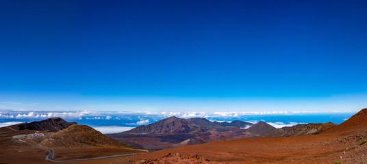Fototapeta na wymiar Scenic panorama of a Haleakala volcano. Clear blue sky white puffy clouds below the horizon and rich red-brown colors of a mountain 
