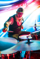 Obraz na płótnie Canvas Cheerful drummer playing on drum set on stage in the color light
