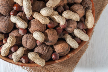 Assorted peanuts, walnuts and hazelnuts. Nuts in a bowl on burlap. White wooden background. Close-up.