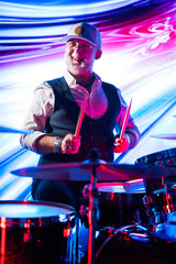 Fototapeta na wymiar Cheerful drummer playing on drum set on stage in the color light