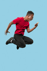 always on mobile. Full length of handsome african young man taking phone while jumping against blue...