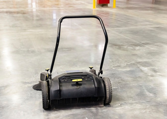 a black sweeper stands on a concrete floor in a factory