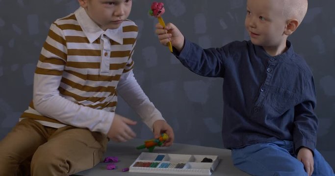 Happy little boy without front tooth in elegant clothes and his little brother mold plasticine figurines. Kids are happy at home. Pre-school development and education