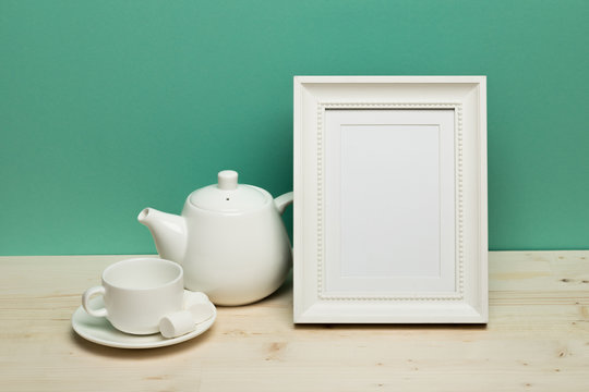 white frame with cup and teapot on white desk near green wall © Fototocam