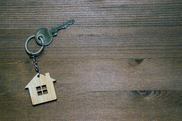 Fototapeta na wymiar The symbol of the house in the form of a keychain with a metal key on a brown vintage wooden background. Copy space.