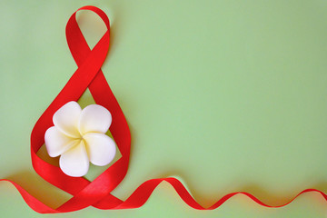 Isolated bright red satin ribbon in the shape of the figure 8 and white with yellow flower on a green background with copy space