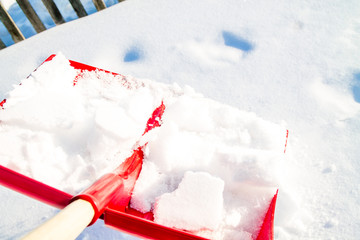 Close up of big red plastic showel in the process of removing the snow in winter