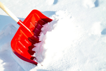 Close up of big red plastic showel in the process of removing the snow in winter