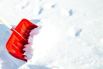 Close up of big red plastic showel in the process of removing the snow in winter