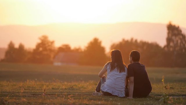 Woman and man sitting together on field admire nature at sunset light, romantic