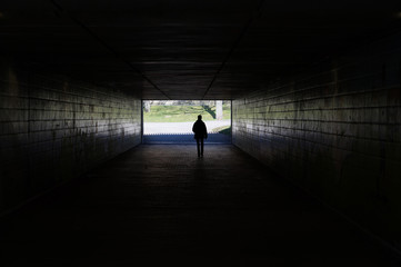 Fototapeta na wymiar silhouette of a person walking through a dark underpass symbolizing light at the end of the tunnel