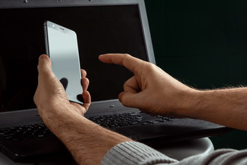 Men's hands holding a smartphone on the background of a laptop. The concept of modern technology. copy space.
