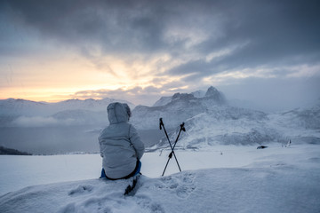 Mountaineer sitting with trekking pole in frosty weather on snow peak