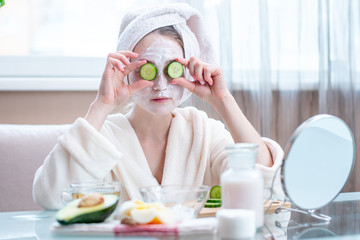 Obraz na płótnie Canvas Beautiful young woman with natural cosmetic mask and cucumber slices on her face. Skin care and Spa treatments at home