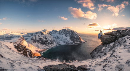 Panorama of Mountaineer sitting on rock on peak mountain of arctic coastline at sunset