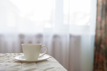 Morning cup of coffee on the background of the bed and the window