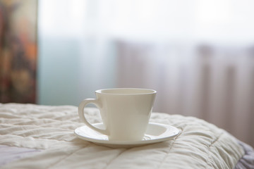 Morning cup of coffee on the background of the bed and the window