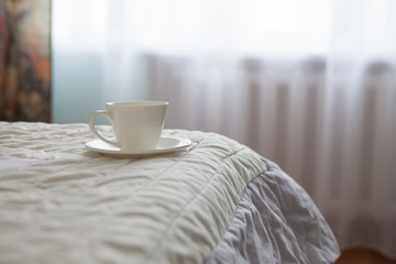Morning cup of coffee on the background of the bed and the window